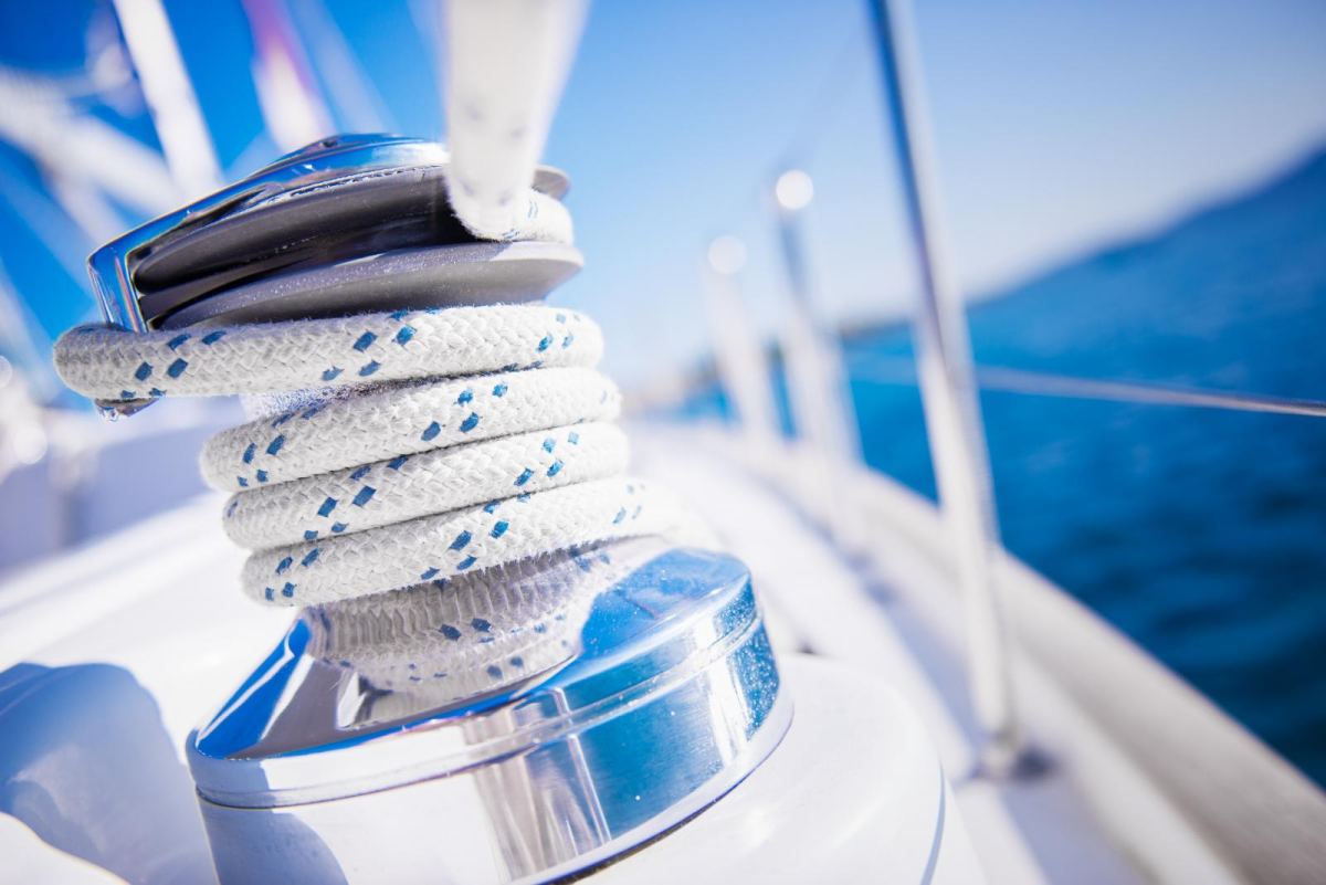 A rope coiled around a chrome winch on the deck of a yacht at sea